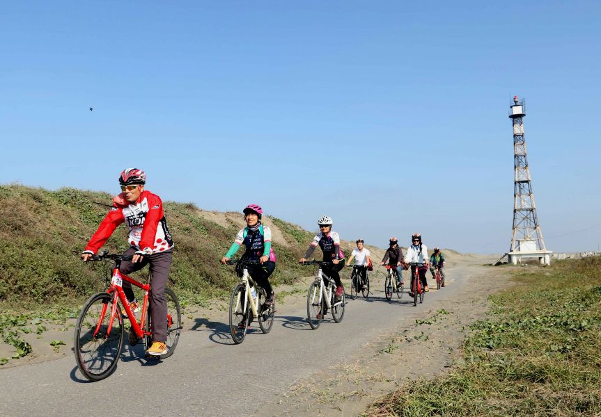 踩線團透過自行車慢旅環島，後為國聖港燈塔。中華民國自行車騎士協會／提供。