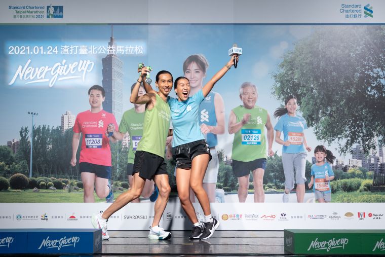 2021渣打臺北公益馬拉松超級戰隊隊長張嘉哲與時尚戰隊隊長莫莉，拿著施華洛世奇獎牌，現場示範完賽時尚照。大會提供