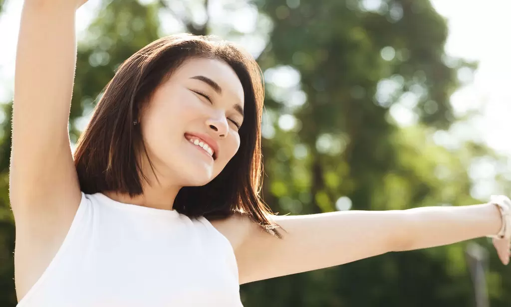 close up asian woman stretching hands up smiling walking park looking carefree happy