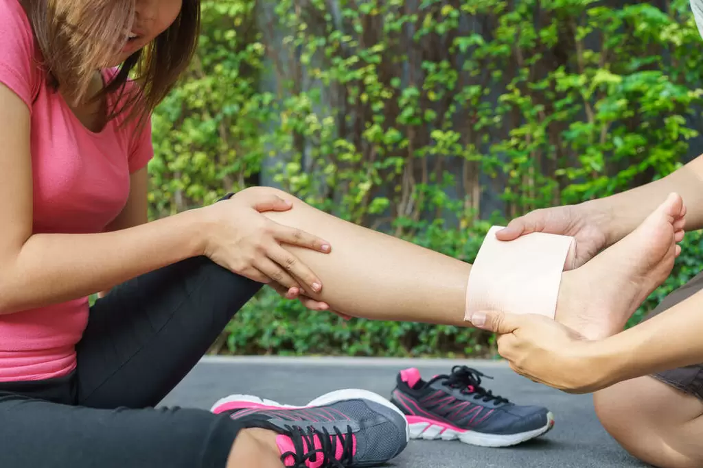 young woman runner ankle being applied bandage by man park injury ankle