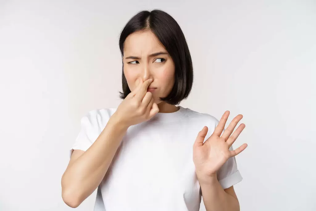 Asian-Girl-Looks-Disgusted-Rejecting-Product-With-Bad-Smell-Shut-Nose-From-Aversion-Cringe-Standing-Against-White-Background